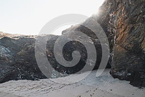 Beach sheltered under a high rock into which the first rays of the sun are streaming in the Odemira region, western Portugal. photo