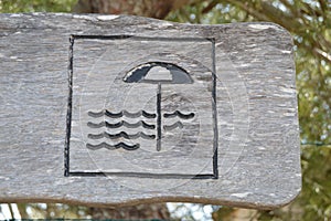 Beach sign on wood. Parasol and waves drawn on wood.