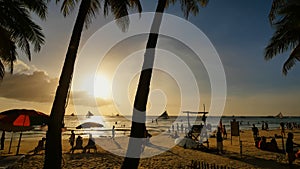 Beach with silhouettes of tourists among palm trees on the island of Boracay. Palm trees in the rays of sunset