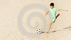 Beach soccer on sand. Boy soccer player kick ball in football match. Sports and recreation for children, summer holidays