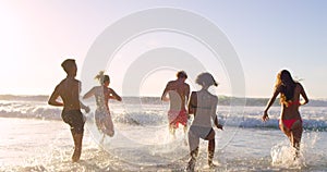 Beach, splash and friends playing in ocean together for fun on travel, vacation or holiday in summer. Back, wave and