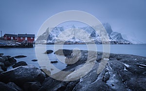 Beach with stones in blurred water, red rorbu and snowy mountains