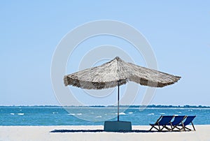 Beach straw umbrella from the sun on the beach with sun beds, on the background of the sea and blue sky,