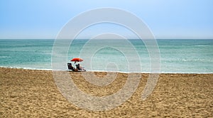 Beach summer couple on vacation holiday relax in the sun on their deck chairs under a red umbrella