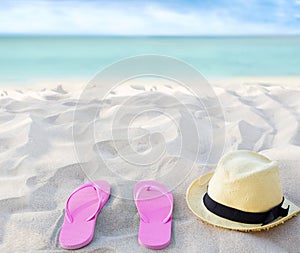 Beach summer holiday background. Flip flops and hat on sand near ocean. Summertime accessories on seaside. Tropical vacation