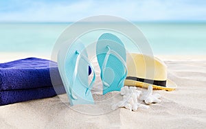 Beach summer holiday background. Flip flops, towels and hat on sand near ocean. Summertime accessories on seaside. Tropical