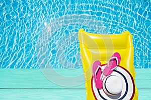 Beach summer holiday background. Inflatable air mattress, flip flops and hat on blue wood floor near swimming pool. Yellow lilo