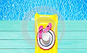 Beach summer holiday background. Inflatable air mattress, flip flops and hat on blue wood floor near swimming pool. Yellow lilo