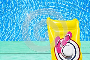 Beach summer holiday background. Inflatable air mattress, flip flops and hat on blue wood floor near swimming pool. Yellow lilo