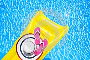 Beach summer holiday background. Inflatable air mattress, flip flops and hat on swimming pool. Yellow lilo and summertime