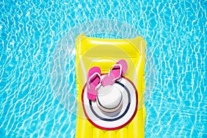 Beach summer holiday background. Inflatable air mattress, flip flops and hat on swimming pool. Yellow lilo and summertime