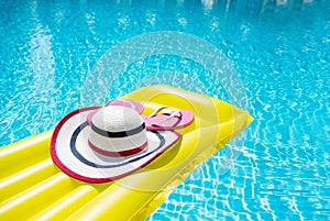 Beach summer holiday background. Inflatable air mattress, flip flops and hat on swimming pool. Yellow lilo and summertime
