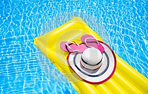 Beach summer holiday background. Inflatable air mattress, flip flops and hat on swimming pool. Yellow lilo and summertime
