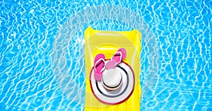 Beach summer holiday background. Inflatable air mattress, flip flops and hat on swimming pool. Yellow lilo and summertime