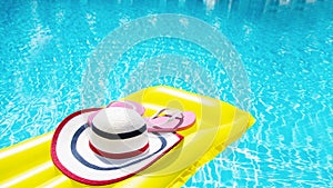 Beach summer holiday background. Inflatable air mattress, flip flops and hat on swimming pool. Yellow lilo and summertime