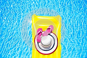 Beach summer holiday background. Inflatable air mattress, flip flops and hat on swimming pool. Yellow lilo and summertime photo