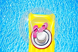 Beach summer holiday background. Inflatable air mattress, flip flops and hat on swimming pool. Yellow lilo and summertime