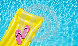 Beach summer holiday background. Inflatable air mattress, flip flops on swimming pool. Yellow lilo and summertime accessories
