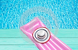 Beach summer holiday background. Inflatable air mattress and hat on blue wooden floor near swimming pool. Pink lilo and summertime