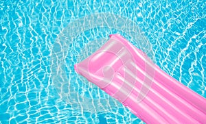 Beach summer holiday background. Inflatable air mattress on swimming pool water. Pink lilo and summertime accessories on poolside