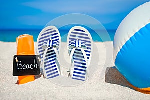 A Beach summer holiday banner background. Flip-flops and hat with a board and ball on the sand near the ocean. Summer accessories