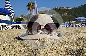 Beach in summer. On the sand lies a woman`s hat with glasses.