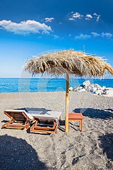 Beach sun beds and straw umbrella on Black Beach in Santorini island, Greece