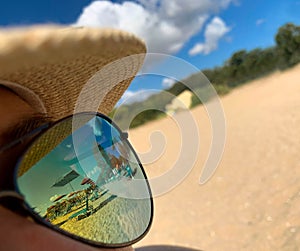 Beach with sun umbrellas and chair lounges reflection in woman sunglasses sitting on the beach at summer