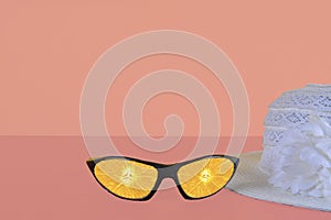 Beach sunglasses summer concept on pink background. Summer hat. Sunglasses reflecting slices of orange. Copy space