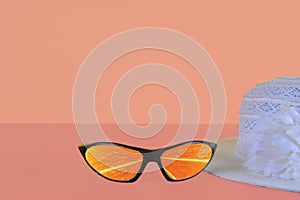 Beach sunglasses summer concept on pink background. Summer hat. Sunglasses reflecting slices of orange. Copy space