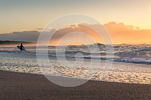 Beach sunrise seascape with surfer at the distance. Seaside summer background