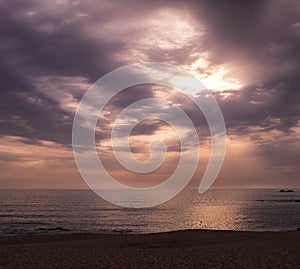 Beach at sunset with rays of sunlight shining through clouds onto ocean. Wide angle.