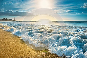 Beach with surf waves and Maspalomas lighthouse on background