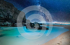 Beach surrounded by the sea and rocks under a bright starry sky at night - perfect for backgrounds