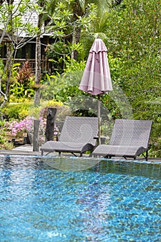 Beach with swimming pool, palm trees, daybeds and umbrella in a tropical garden near sea, Thailand