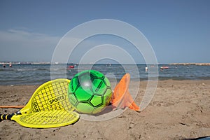 Beach tennis racket and ball, and beach volleyball ball on tne beach
