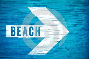 Beach text sign written on a white directional arrow pointing towards right manually painted on a blue wooden signboard photo