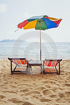 Beach in Thailand, two deck chairs and colorful umbrella