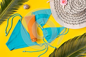 Beach theme on the yellow background. Sunscreen, hat, palm leaves, swimsuit  on the yellow background