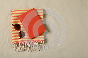 Beach towel, book and sunglasses on sand, top view. Space for text