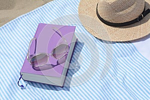 Beach towel with book, sunglasses and straw hat on sand