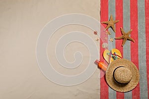 Beach towel, hat, sunscreen, starfishes, sea shells and flip flops on sand, flat lay