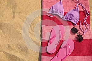Beach towel with slippers, sunglasses and swimsuit on sand, top view. Space for text