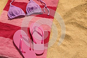 Beach towel with slippers and swimsuit on sand, space for text