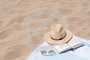 Beach towel with straw hat, sunglasses and book on sand. Space for text
