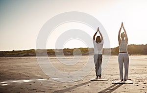 The beach is tranquil, add yoga and it becomes liberating. Rearview shot of an unrecognizable couple practising yoga on