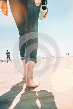 Beach travel - woman in a jeanse walking on sand beach leaving footprints in the sand. Closeup detail of female feet and