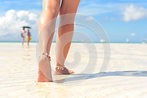 Beach travel - woman walking on sand beach. Closeup detail of female feet and golden sand.