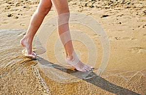 Beach travel - young girl walking on sand beach leaving footprints in the sand. Closeup detail of female feet and golden sand