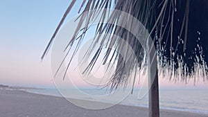 Beach umbrella of dry palm leaves on a deserted beach in the middle of the sunset,dolly shot,blurred background